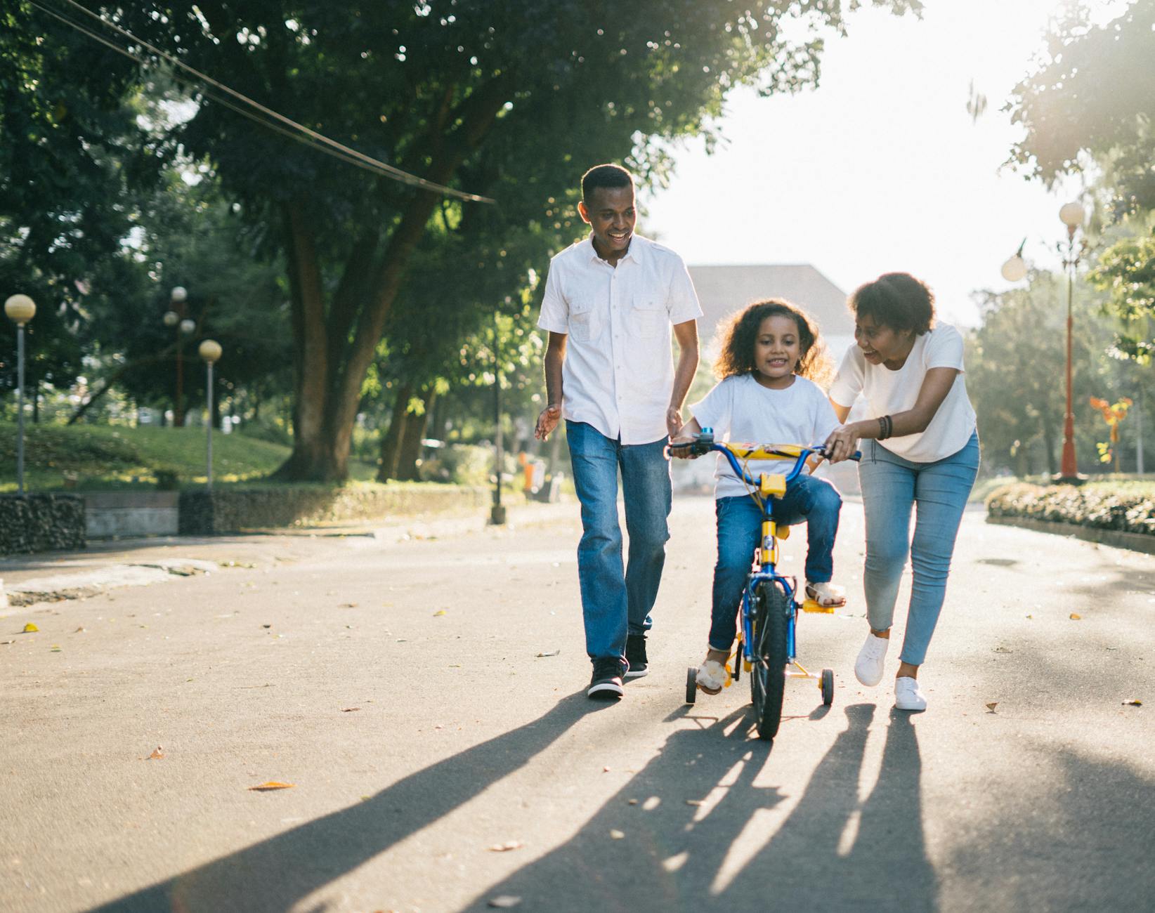 Mom and dad helping their tween learn to ride a bicycle outdoors, showing guidance, support, and family connection.