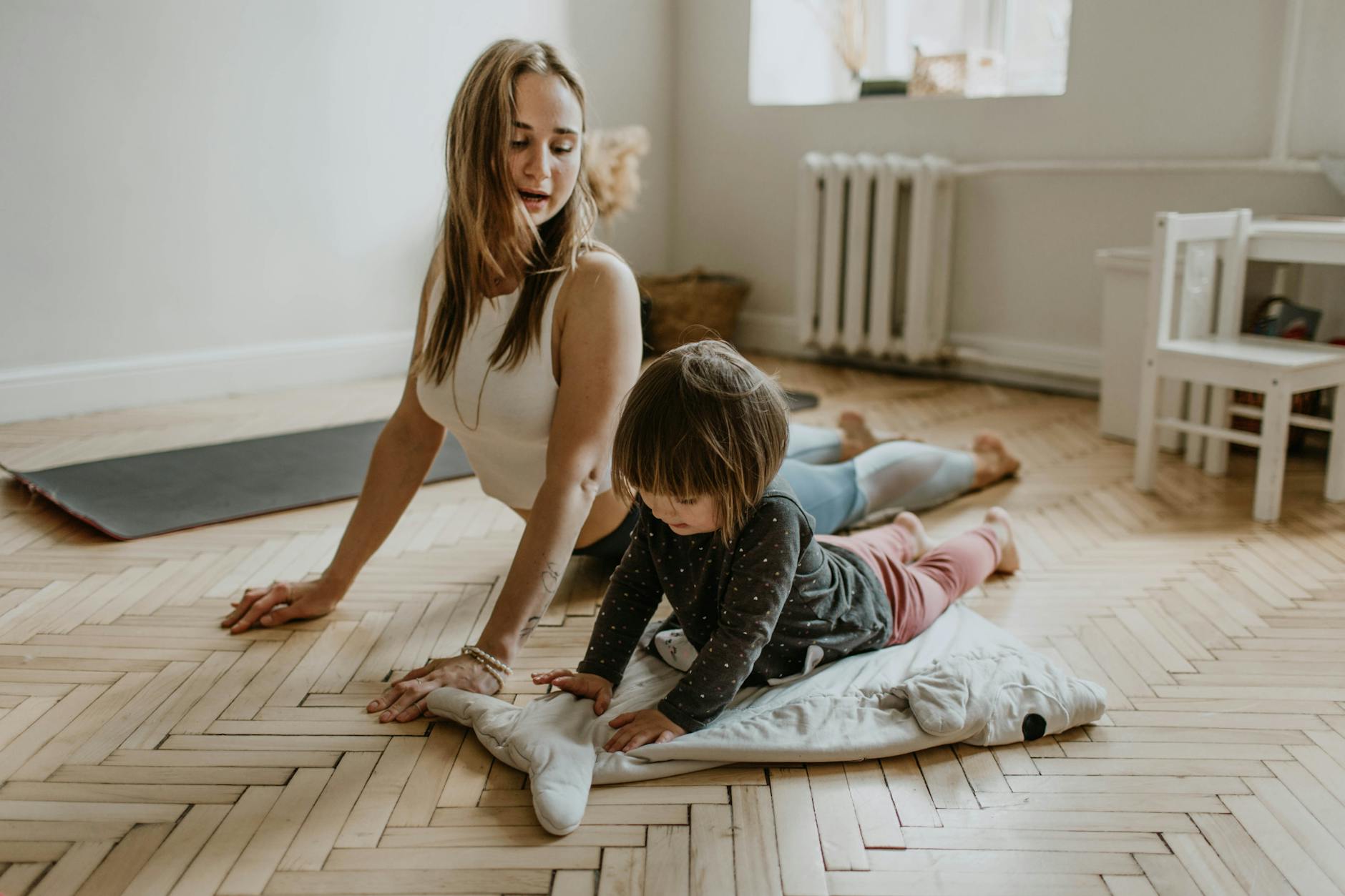 Girl doing yoga with her mother at home, engaging in a shared activity and bonding.