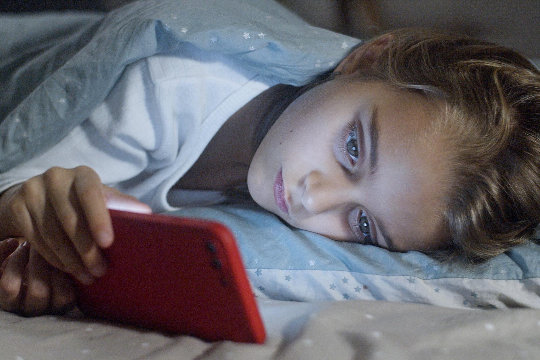 Young child using mobile phone before sleep, showing risks of excessive screen time in kids.