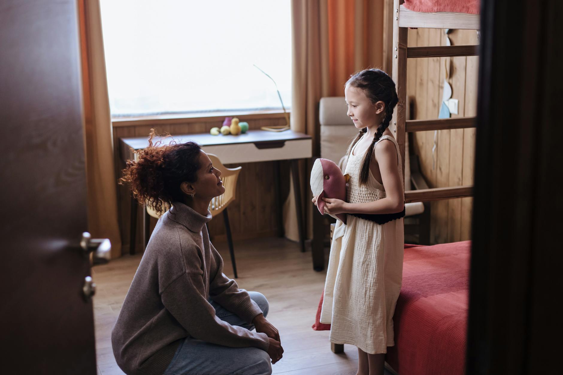 Parent kneeling to make eye contact with tween daughter while listening attentively, showing empathy and understanding.