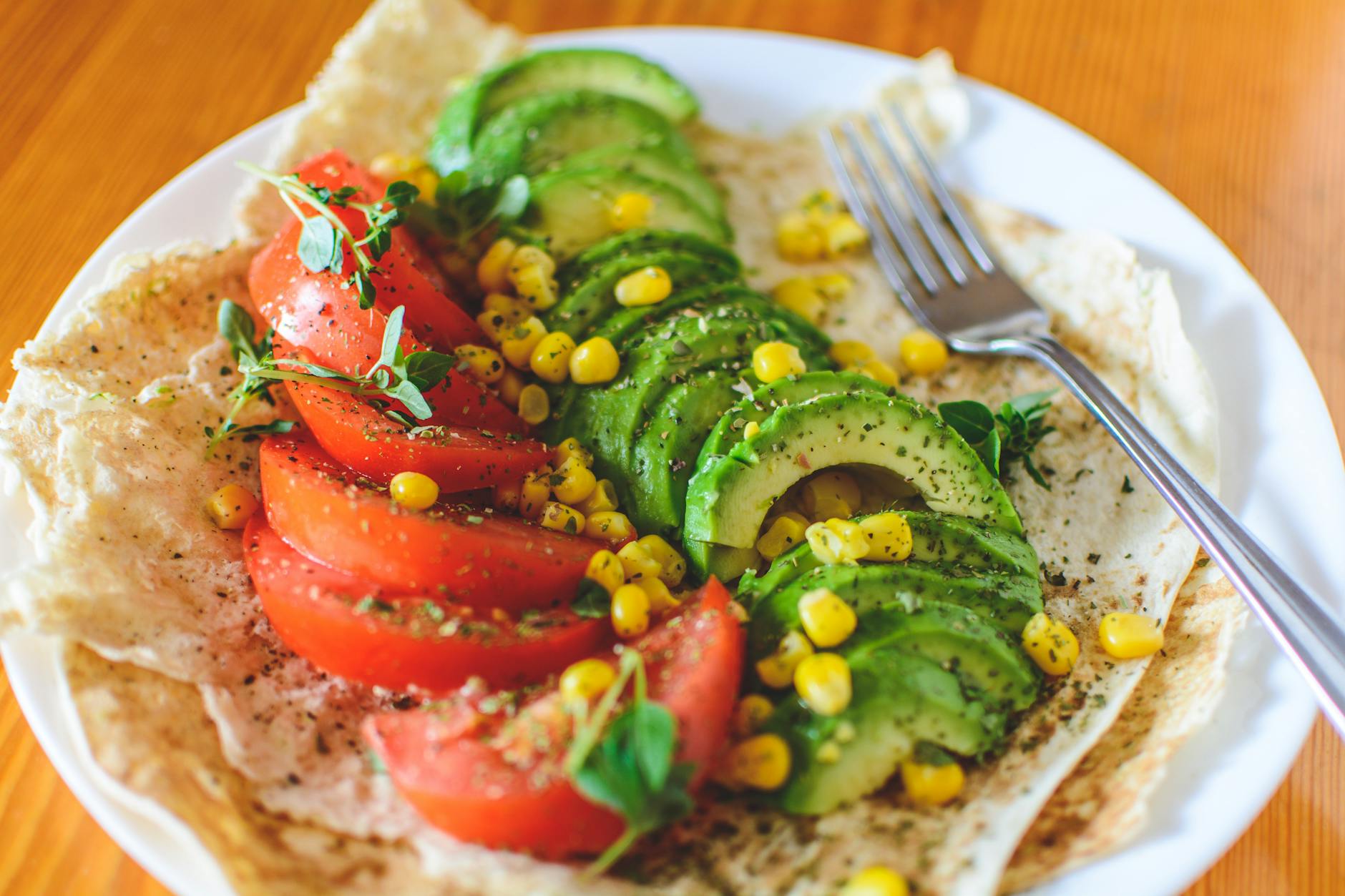 Corn tortilla topped with avocado, tomato slices, and fresh greens, a healthy and colorful snack or light meal.