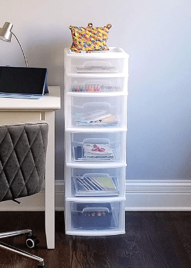 Transparent plastic drawer tower filled with small toys, figures, and art supplies.