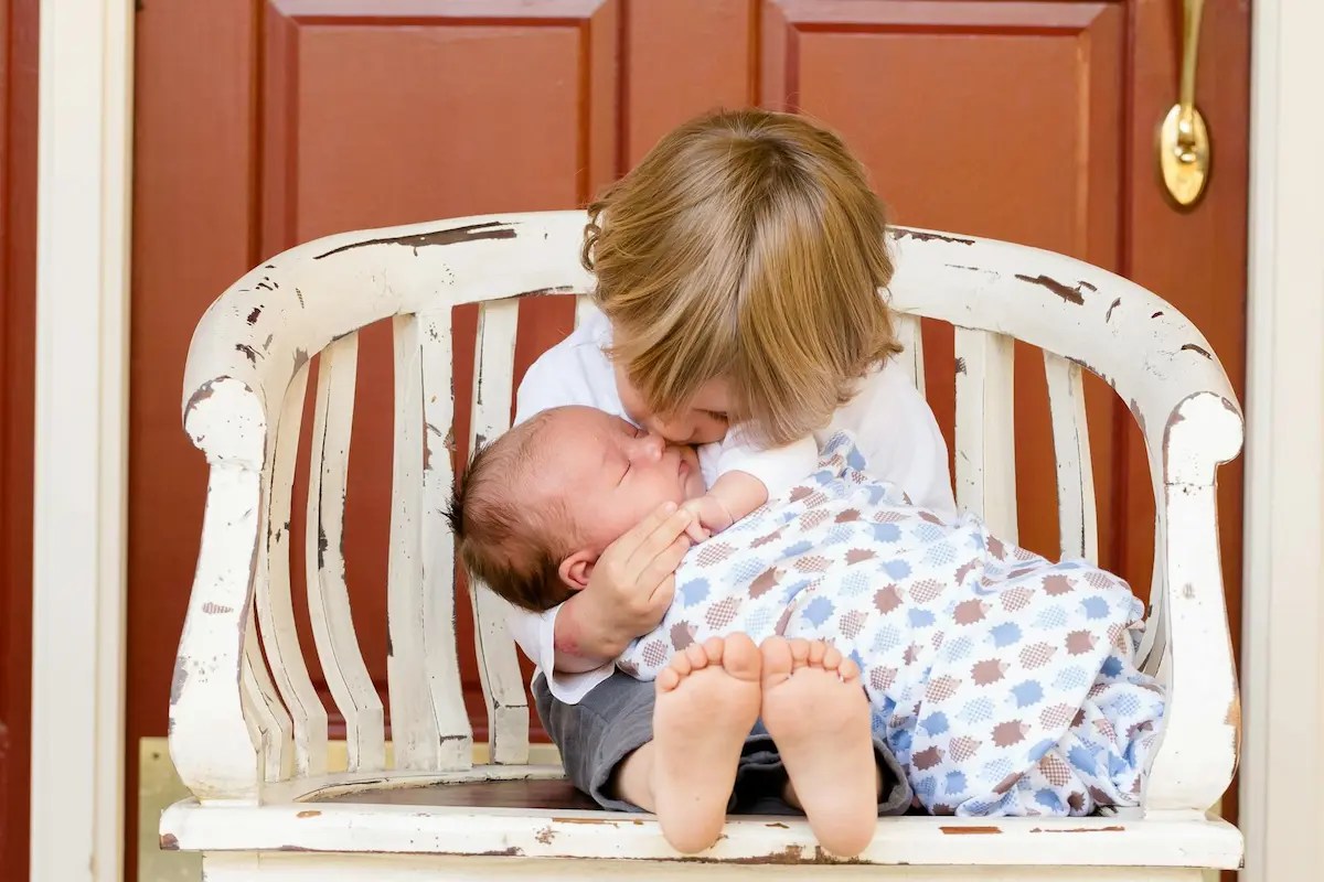 Toddler holding and kissing baby sibling, illustrating the bond between siblings with a significant age gap.