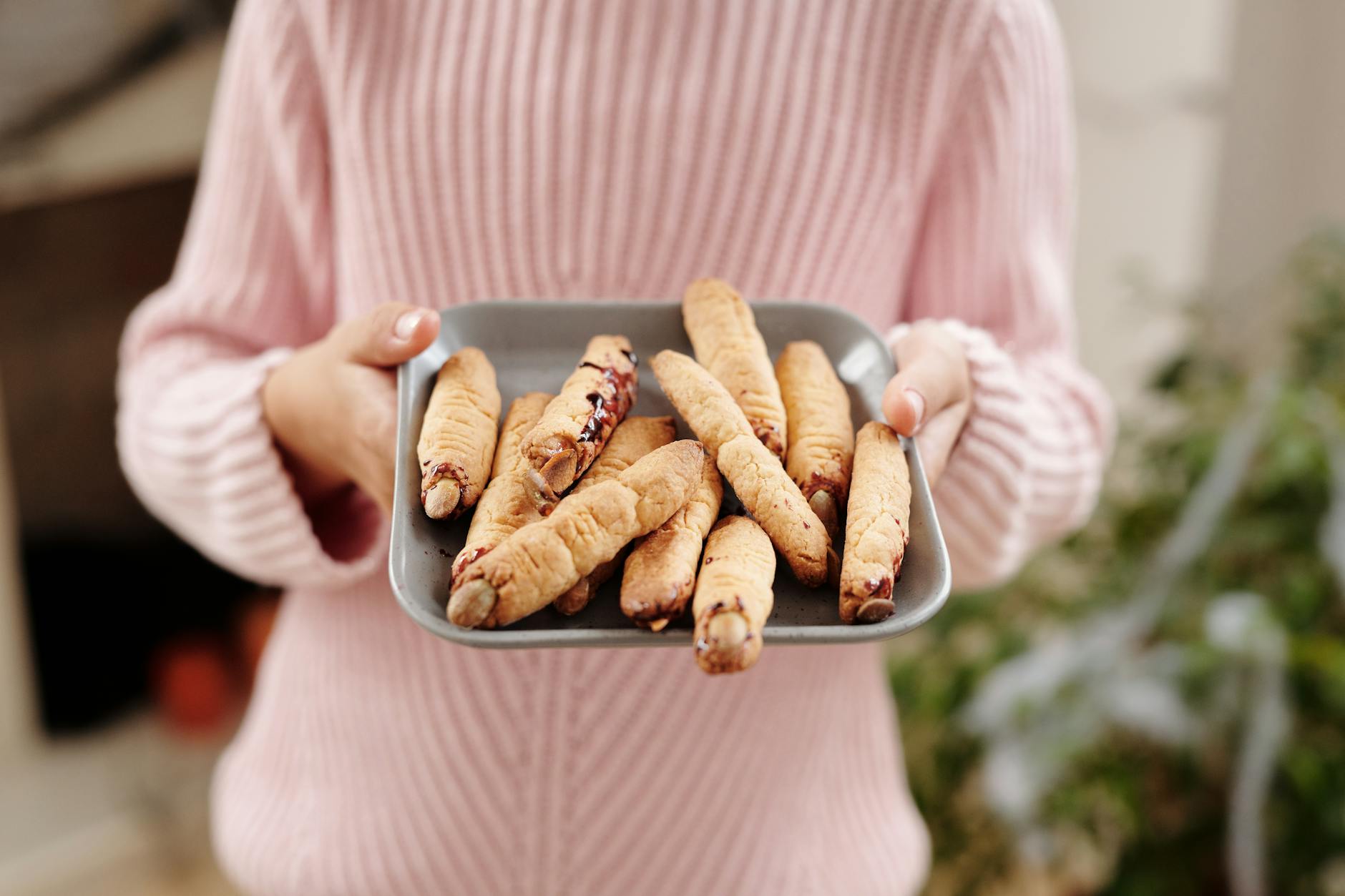 person holding a tray of bread with witch fingers design